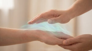 Mains d'un praticien survolant doucement le poignet d'une personne avec une aura lumineuse verte représentant le soin.